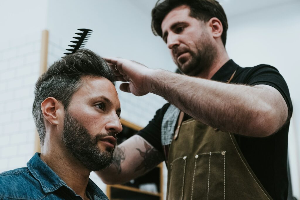 Barber combing hair to man in salon