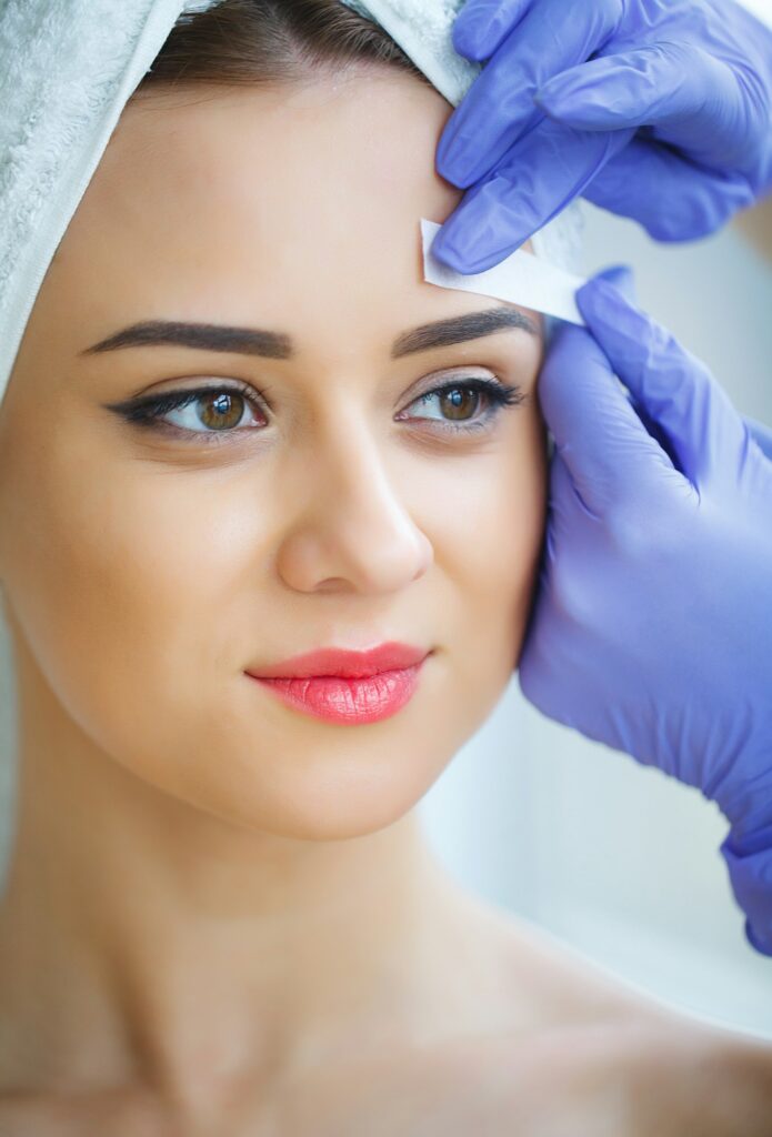 Beautician waxing young woman's eyebrows in spa center