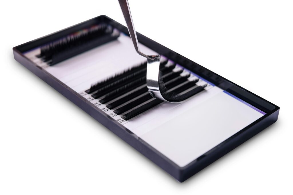 Close-up image of tweezers holding an eyelash extension above a tray