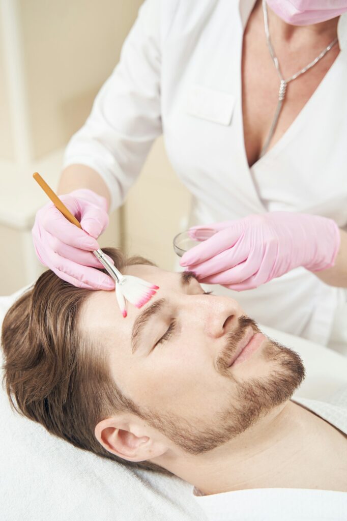 Cosmetologist performing peeling while applying chemical on man face