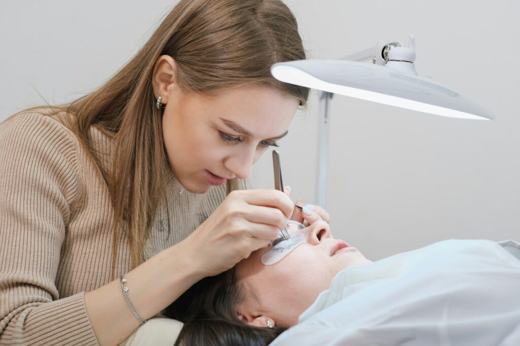 young woman beautician holding tweezers with false lash during lash extension procedure