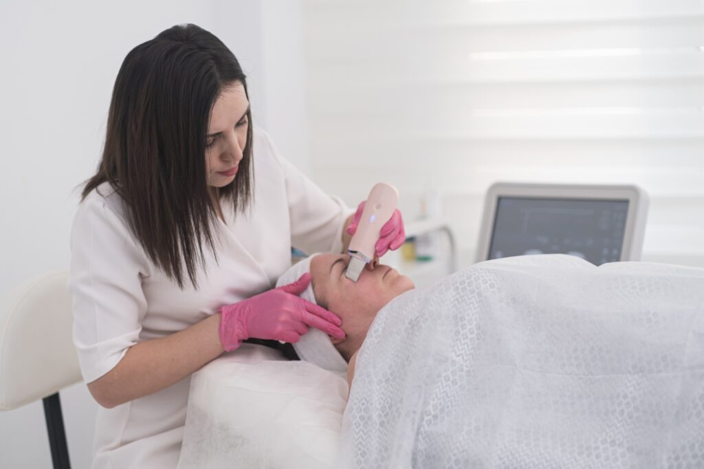 beautician in gloves uses ultrasonic spatula for facial skin scrubbing and cleansing. ultrasound