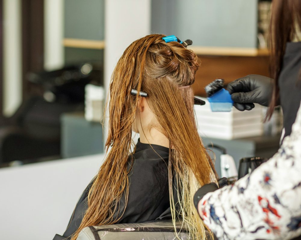 Hairdresser applies color to long hair. Young woman in beauty salon. Image change concept, hair care